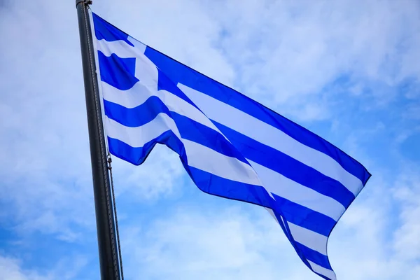 Waving flag of Greece on flagpole. Blue sky with few clouds background. — Stock Photo, Image