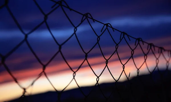 Забор из проволочной сетки на силуэтах шестов на фоне неба размывается на закате — стоковое фото