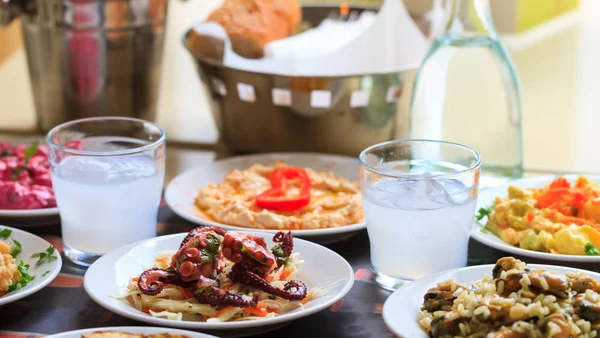 Ouzo in short glasses with ice. Appetizers of seafood in plates. Blur backdrop, close up, details — Stock Photo, Image