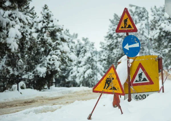 En construcción signos en la nieve. Camino nevado y bosque de fondo . — Foto de Stock