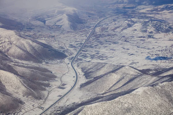 Karlı dağlar arka plan, otoyol aralarında. Uçak penceresinden hava fotoğraf. — Stok fotoğraf