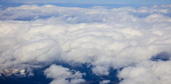 Biały chmury ciężki tło wiszące na błękitne niebo nad górskim. Zdjęcie lotnicze z okna samolotu. — Zdjęcie stockowe