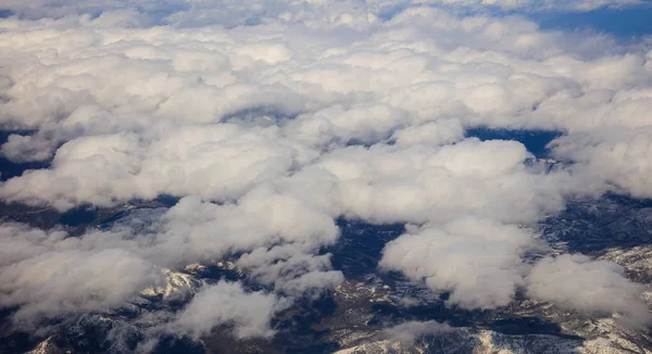Vita tunga moln bakgrunden hänger på blå himmel över berget. Flygfoto från planets fönster. — Stockfoto