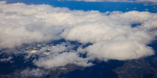 Bianco nuvole pesanti sfondo appeso sul cielo blu sopra la montagna. Foto aerea dalla finestra dell'aereo . — Foto Stock