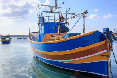 Geleneksel balıkçı teknesi, luzzu, Marsaxlokk, Malta adlı bağlantılı. Mavi gökyüzü bulutlar ve köy arka plan ile. Görünümü kapatın.