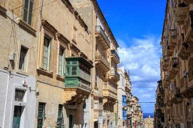 Malta Valletta, geleneksel kumtaşı binalar ile balkonlarda renkli ahşap pencere eşiği. Bulutlar ve deniz arka plan mavi gökyüzü.