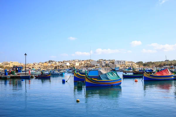 MARSAXLOKK tarihi liman Malta'da ahşap tekneler dolu. Mavi gökyüzü ve köy arka plan. — Stok fotoğraf
