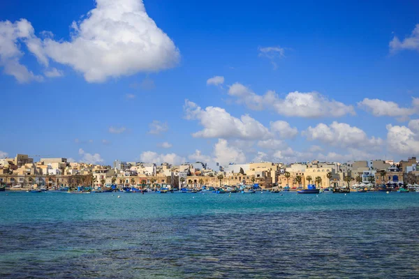 MARSAXLOKK tarihi liman Malta teknelerle dolu. Kaç beyaz bulutlar ve köy arka plan mavi gökyüzü. Panoramik görünüm. — Stok fotoğraf