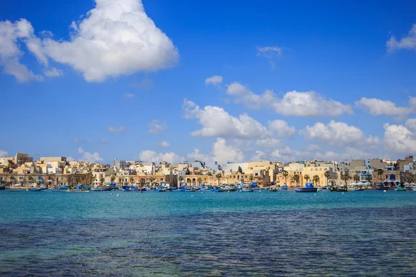 Marsaxlokk historic port full of boats in Malta. Blue sky with few white clouds and village background. Panoramic view. — Stock Photo, Image