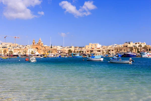 Puerto histórico de Marsaxlokk con muchos barcos en mar transparente, Malta. Cielo azul y fondo del pueblo . —  Fotos de Stock