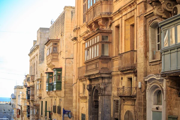 Malta Valletta, traditionele zandstenen gebouwen met kleurrijke houten ramen op balkons. Blauwe hemel met wolken en achtergrond van de zee. — Stockfoto