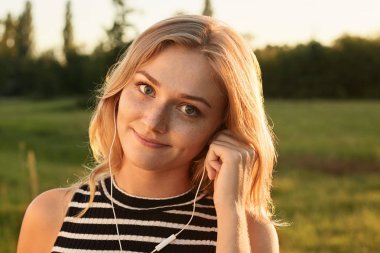 Güzel bir kız sihirli gülümsemeyle straightly kamera seyir ve onun kulaklık ile müzik dinlemek. Elini onun kulaklık dokunmadan bir kız.