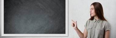 Akıllı bir güzel kız öğrenci sınıfta kameraya yan ve işaret parmağını, blackboard ile ayakta