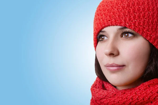 Um rosto de uma mulher atraente. Uma jovem bonita com grandes olhos castanhos com pestanas longas e lábios expressivos usando chapéu vermelho e cachecol olhando à distância e sonhando com férias de inverno — Fotografia de Stock