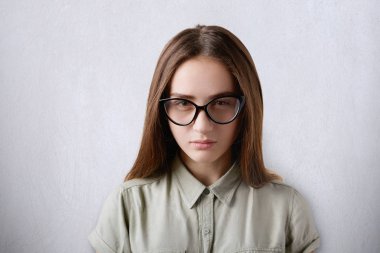 Gizemli ve kurnaz göz doğrudan kameraya olan gri arka plan üzerinde çekici kahverengi gözlü kızı siyah düz saçlı giyen gömlek ve büyük gözlük bir close-up izole