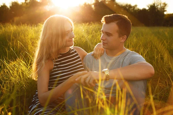 Sebuah foto pasangan muda duduk di rumput saling memandang dengan cinta saling berpegangan tangan santai di luar ruangan. Konsep romantis. Pasangan muda yang bahagia. Musim panas waktu, sinar matahari, cuaca yang bagus — Stok Foto