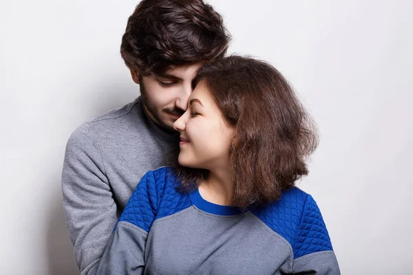 Pessoas, amor e relações. Um casal sírio em pé sobre fundo branco. Homem barbudo na moda vestindo camisola cinza abraçando sua linda garota. Um lindo casal tendo descanso sendo feliz — Fotografia de Stock