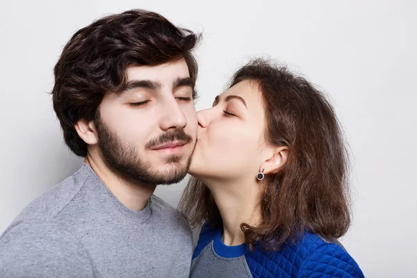 Casal romântico amoroso. Uma morena bonita beijando seu namorado barbudo em seu queixo. Um casal feliz fechando os olhos de prazer isolado sobre fundo branco ter noite romântica — Fotografia de Stock