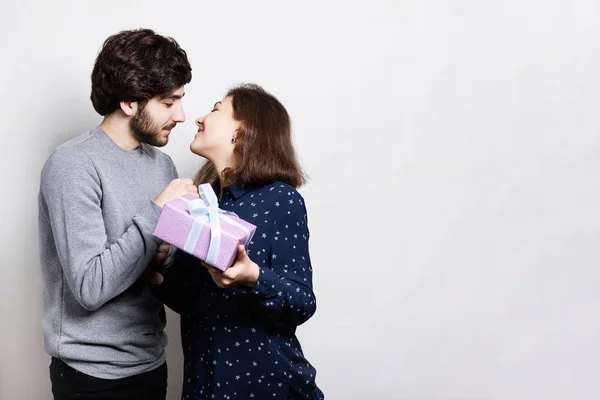 Bonito jovem dando presente à bela mulher em casa. Uma rapariga vai beijar o namorado para agradecer por um presente. Belo jovem casal está comemorando em casa. Verdadeiro amor entre pessoas — Fotografia de Stock