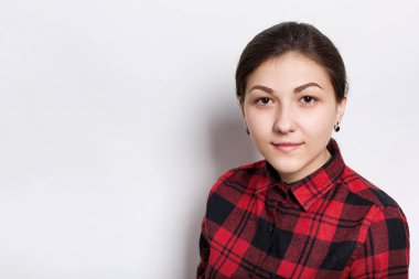 Örgülü saçlı kahverengi gözlü ve beyaz arka plan üzerinde izole kamera bakarak ciddi kırmızı ekose desenli gömlek giymiş ifade kaşları olan bir genç esmer kadın. Genç hippi kız Close-Up