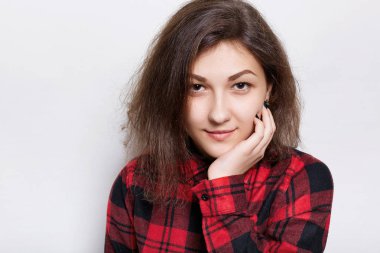 Beyaz arka plan üzerinde izole kamera içine emin seyir çene üzerinde elini tutarak kırmızı işaretli gömlekli güzel genç esmer kadın. Güzel kız kendinden emin bir ifadesidir