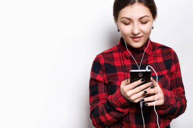 Kişi, yaşam tarzı ve teknoloji kavramı. Kulaklık takmış çekici erkek portresi. Oldukça şık giyen genç kız gülümseyerek gömlek cep telefonu onun en sevdiği parçayı dinlerken tutarak kontrol 