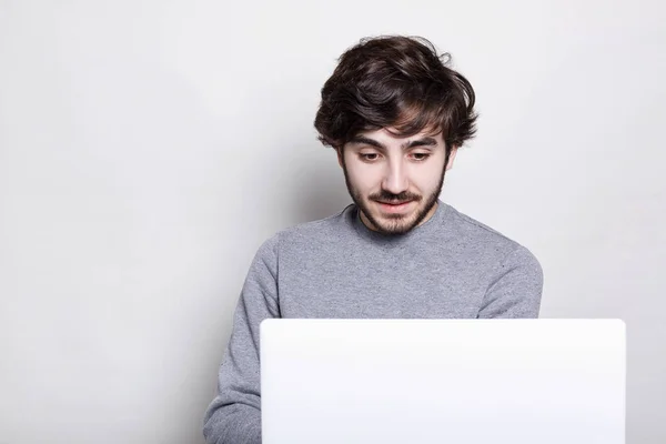 Porträt eines jungen, außergewöhnlich aussehenden Mannes mit dunklem Bart, der isoliert auf seinem Laptop vor weißem Hintergrund arbeitet. Erstaunter Mann erhält Nachrichten — Stockfoto