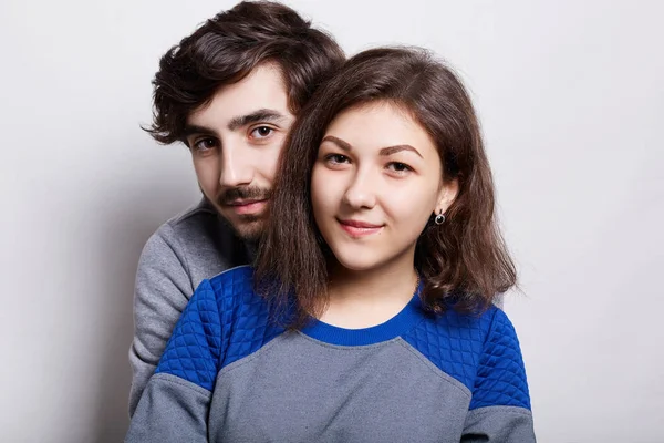 Pessoas e relacionamentos. Casal jovem em pé perto da parede branca. Um tipo hipster com barba a bater na namorada a abraçá-la. Uma morena bonita sendo feliz de ficar perto de seu amante — Fotografia de Stock