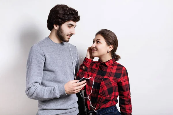 Pareja de jóvenes adultos escuchando música juntos mirándose. Pareja feliz con auriculares compartiendo música desde un teléfono inteligente. Tecnología, personas, concepto de relaciones . — Foto de Stock