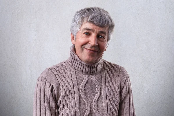 Personas y emociones. Retrato de un anciano de pelo gris y ojos brillantes llenos de felicidad que tiene una sonrisa agradable mirando a la cámara vestida con suéter aislado sobre fondo blanco —  Fotos de Stock