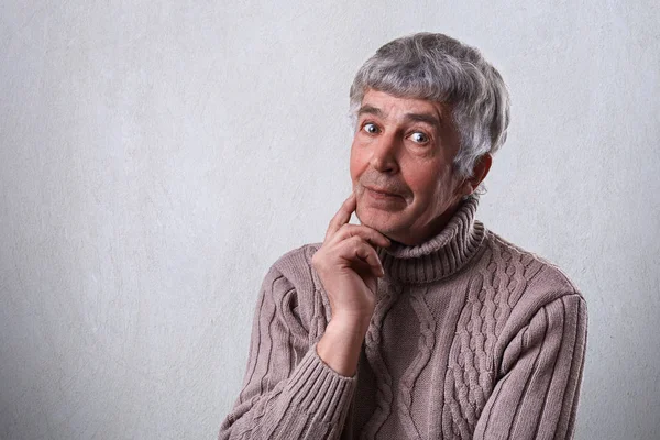 Finding perfect solution. Mature handsome man with gray hair and wrinkles holding his finger on cheek looking thoughtful and having mysterious expression while standing against white background — Stock Photo, Image