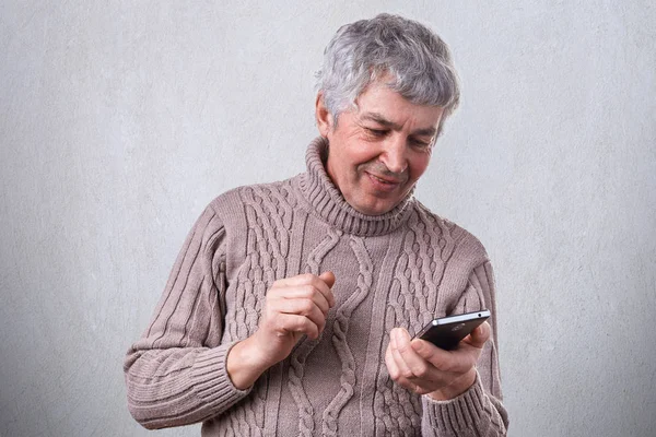 Щасливий усміхнений зрілий чоловік тримає свій смартфон в руках приємно отримувати повідомлення від свого сина. Технології, люди, спосіб життя та концепція спілкування. Щасливий старший чоловік має відеодзвінок — стокове фото