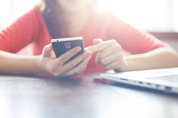 Modernes Smartphone in Frauenhand. junge Frau mit elektronischem Gerät, mit kostenlosem Wi-Fi, Video oder Bilder online über soziale Netzwerke ansehen, während sie am Tisch neben ihrem Laptop sitzt — Stockfoto