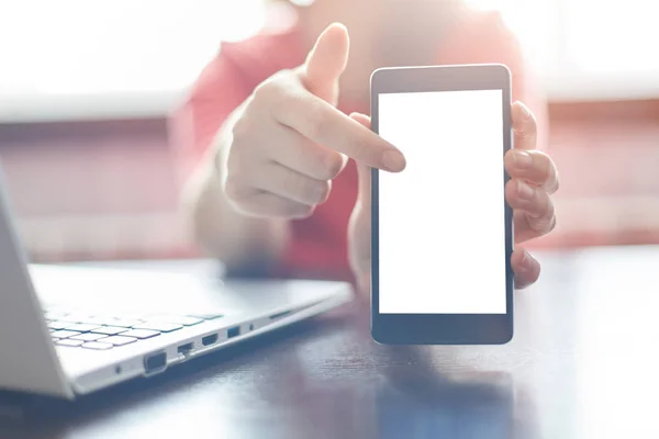 Närbild av kvinnliga händer som håller tom smartphone, pekar ett finger på skärmen kopia utrymme för din annons. En kvinna som arbetar vid bordet med sin laptop visar hennes mobiltelefon — Stockfoto