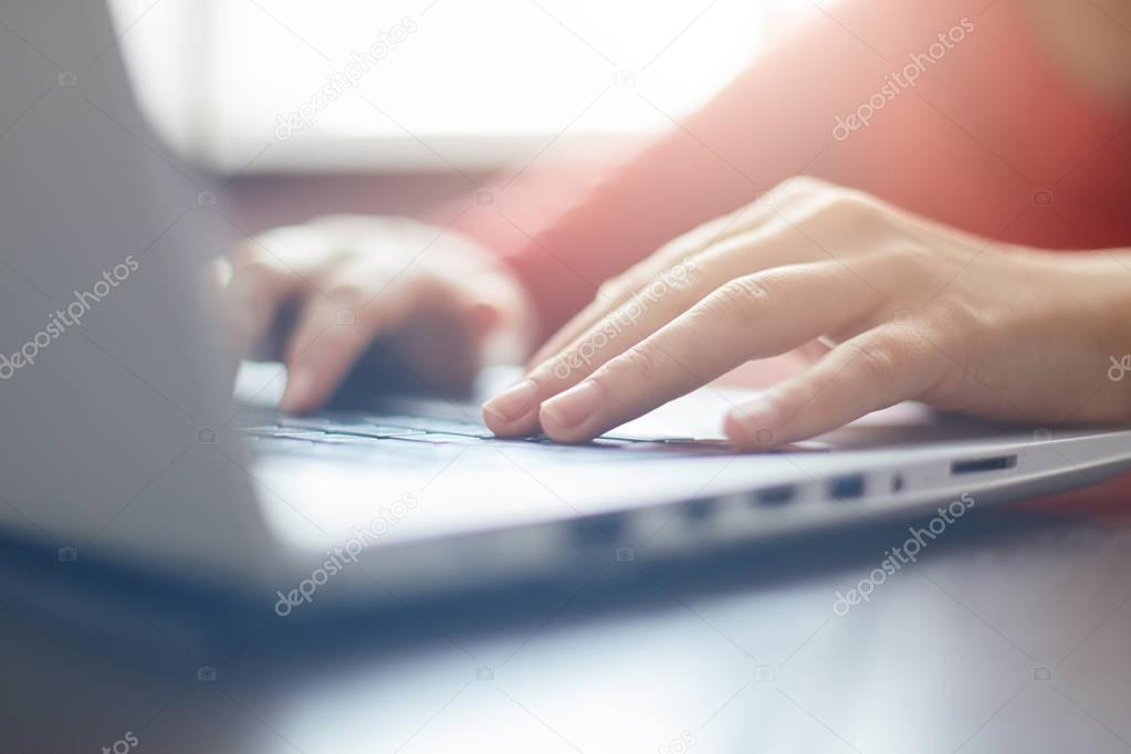 Close-up portrait of woman's hands typing on laptop sitting at the table. Female businesswoman working on-line via laptop computer sitting in front open net-book. Selective focus on fingers