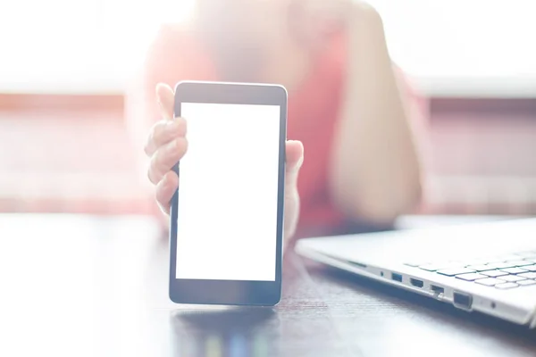 A cropped shot of female holding cell phone with blank screen for your promotional content. Girl showing something interesting on cell phone while sitting at table near her laptop. — Stock Photo, Image