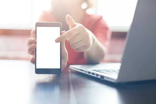 Close up shot of female hands holding smart phone with blank copy space screen for your text or information content pointing with a finger at the screen. Young fremale using smartphone and laptop — Stock Photo, Image