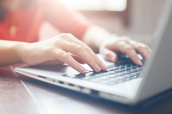 Frauen tippen auf der Tastatur des Laptops, surfen im Internet und schreiben Freunden SMS über soziale Netzwerke, sitzen drinnen am Holztisch. Technik- und Kommunikationskonzept / selektiver Fokus. — Stockfoto