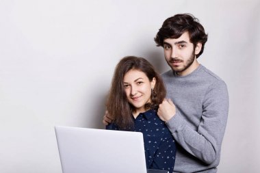 Bir mutlu bir adam ve beyaz arka plan üzerinde izole kamera doğrudan bakarak dizüstü bilgisayar ile yan duran kadın. Sakal ayakta arkasında onun kız arkadaşı enjoing modern teknolojiler ile şık adam. 