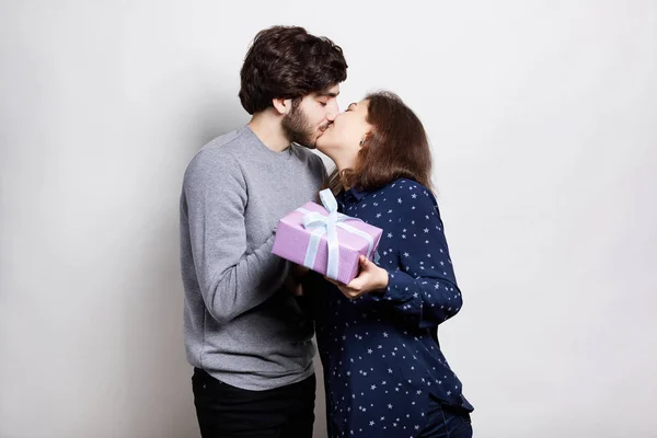 Casal feliz segurando caixa de presente rosa beijando uns aos outros apaixonadamente. Amor, relacionamento, namoro, amantes, tiro conceito, no fundo branco. Adorável jovem hipster casal beijando . — Fotografia de Stock