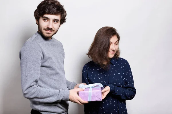 Um casal feliz com presente. Um tipo hipster a apresentar um presente à namorada a olhar para o lado. Jovens machos e fêmeas isolados sobre fundo branco. Pessoas e conceito de relacionamento . — Fotografia de Stock