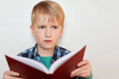 Mavi gözlü ve sarışın çekici okul çocuğu Close-Up düşünceli ifade beyaz duvarının yakınında duran bir şey hakkında hayal sahip onun elinde bir kitap tutan ekose desenli gömlek giymiş