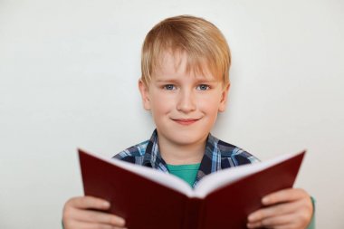 Sarı saçlar ve doğrudan kameraya bakarak mutlu ifade sahip beyaz arka plan üzerinde duran onun elinde bir kitap tutan mavi gözlü yakışıklı küçük çocuk portresi. Eğitim kavramı.