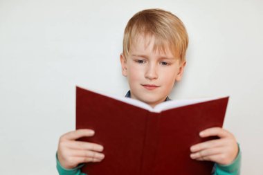 Sarı saçlı ve mavi gözleri kırmızı tutan bir küçük tatlı çocuk hikayeleri ilginç kitap okuma açıldı. Yedi yaşında çocuk büyük bir ilgi ile bir kitap okuma. İnsanlar ve yaşam tarzı kavramı.
