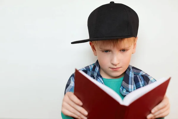 可爱的小男孩和蓝色的眼睛，黑色的帽子，格纹的衬衫读一本书，在备课与严肃的表情看着这本书。人与教育思想. — 图库照片