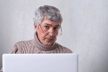 Ev ciddi bir ifadeyle kameraya bakıyor olurken ile bir dizüstü bilgisayar çalışma gözlük takan bir emin olgun iş adamı. Kişi, yaşam tarzı ve teknoloji kavramı.