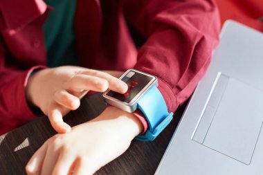 Çocuğun elleri akıllı saat takan bir close-up. Elektronik izlemek dokunmak. Giyilebilir gadget kavramı. Gösterme zamanı. Belgili tanımlık laptop yanında otururken smartwatch kullanarak. Teknoloji ve insan kavramı.