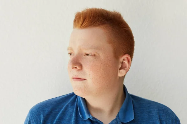 Un portrait latéral d'un garçon rousse réfléchi avec une coiffure à la mode et des taches de rousseur portant une chemise bleue décontractée regardant de côté isolé sur fond blanc. Un gars élégant posant en studio . — Photo