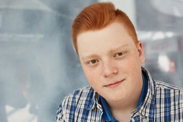 A close-up of positive guy with round face having freckles and stylish red hair dressed in fashionable checked shirt looking directly into camera. — Stock Photo, Image