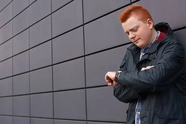 Szép redhead vízszintes portréja szeplős fiú és stílusos fodrász jelentő nézett órájára várakozás-re jönni barátnője fekete fal mellett fekete kabát öltözött — Stock Fotó